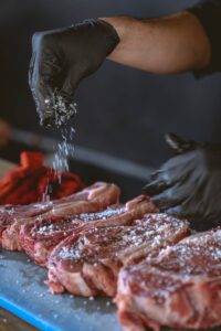 A chef seasons raw steaks with sea salt, perfecting the preparation process.